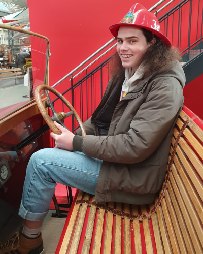 Nicolas steers an early fire department vehicle with appropriate headwear and facial expression